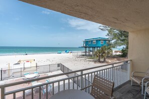 Un balcon donnant sur une plage, un immeuble bleu et une table avec des chaises.