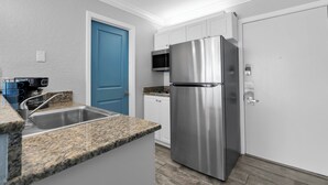 Cocina con encimeras de granito, electrodomésticos de acero inoxidable, gabinetes blancos, una puerta azul y un microondas.