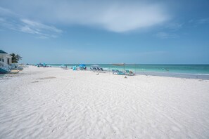 A beach with white sand, a few umbrellas, and lounge chairs. - Beachfront Studio on Anna Maria Island (Bradenton Beach)