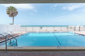 A swimming pool with a view of the ocean, a palm tree, and a white fence. - Beachfront Studio on Anna Maria Island (Bradenton Beach)