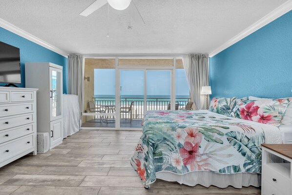 A bedroom with a large bed, a dresser, a ceiling fan, and a view of the ocean through a sliding glass door. - Beachfront Studio on Anna Maria Island (Bradenton Beach)