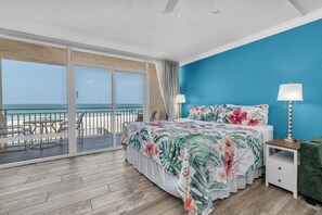 A bedroom with a large bed, a nightstand, a green chair, and a balcony with a view of the beach. - Beachfront Studio on Anna Maria Island (Bradenton Beach)
