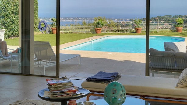 En pool med udsigt over havet, et sofabord med bøger og en vase, samt en sofa med et tæppe.