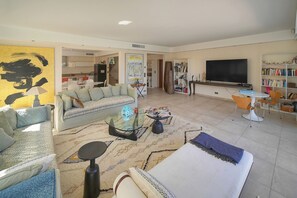 Ein modernes Wohnzimmer mit Sofa, Couchtisch, Fernseher, Bücherregal und einer Treppe, die in die Küche führt.