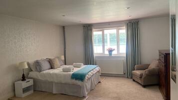 Een slaapkamer met een bed, nachtkastje, lamp, raam met gordijnen, radiator en een stoel.