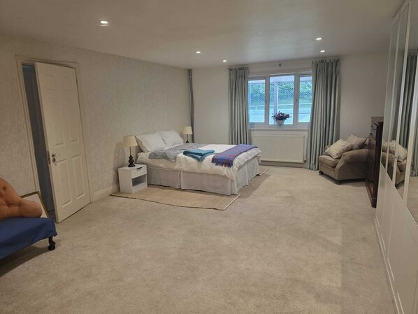 A bedroom with a bed, bedside tables, a chair, a window with curtains, and a radiator.