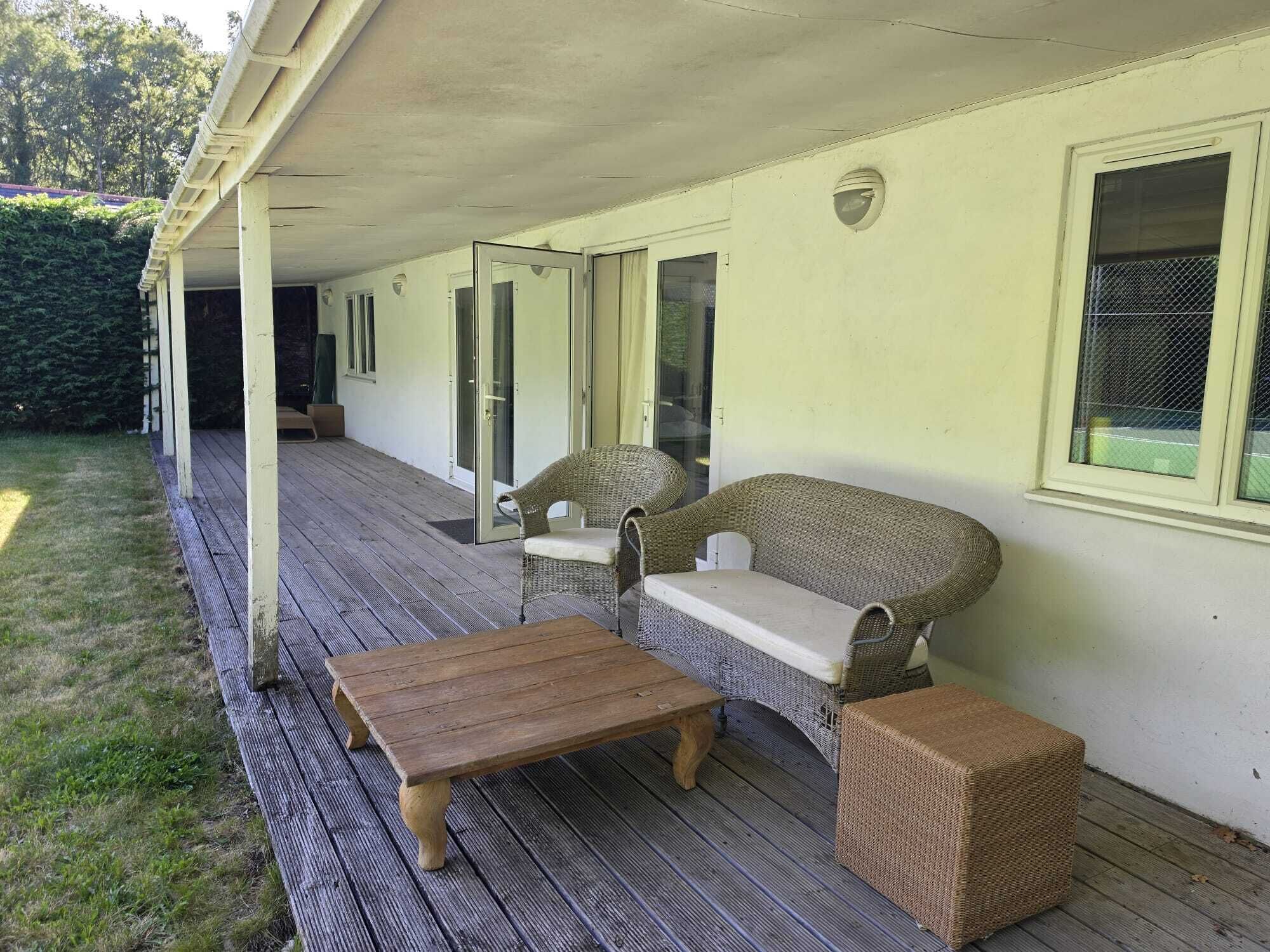 A covered outdoor seating area with a wooden table and wicker furniture.