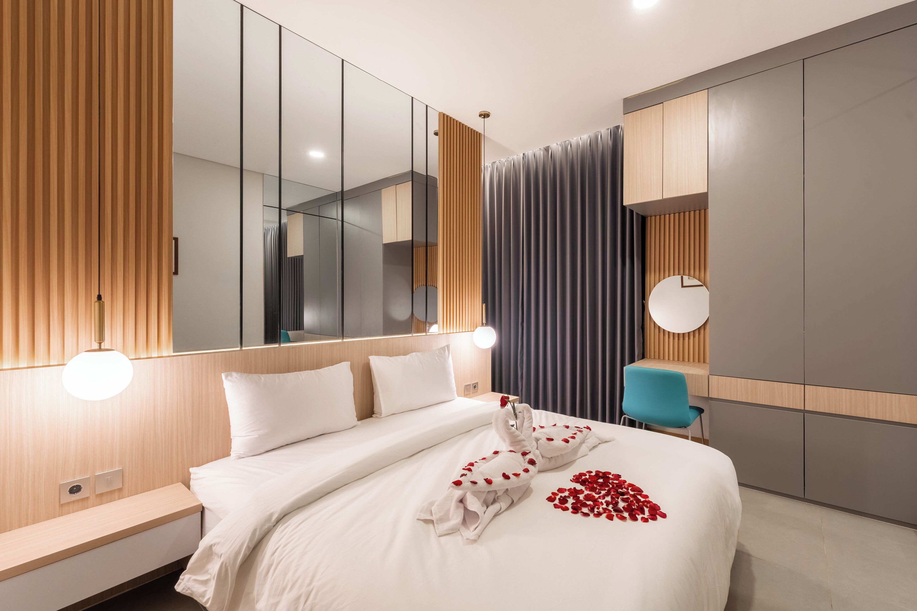 A modern hotel room with a large bed, a bedside table, a chair, and a wardrobe.