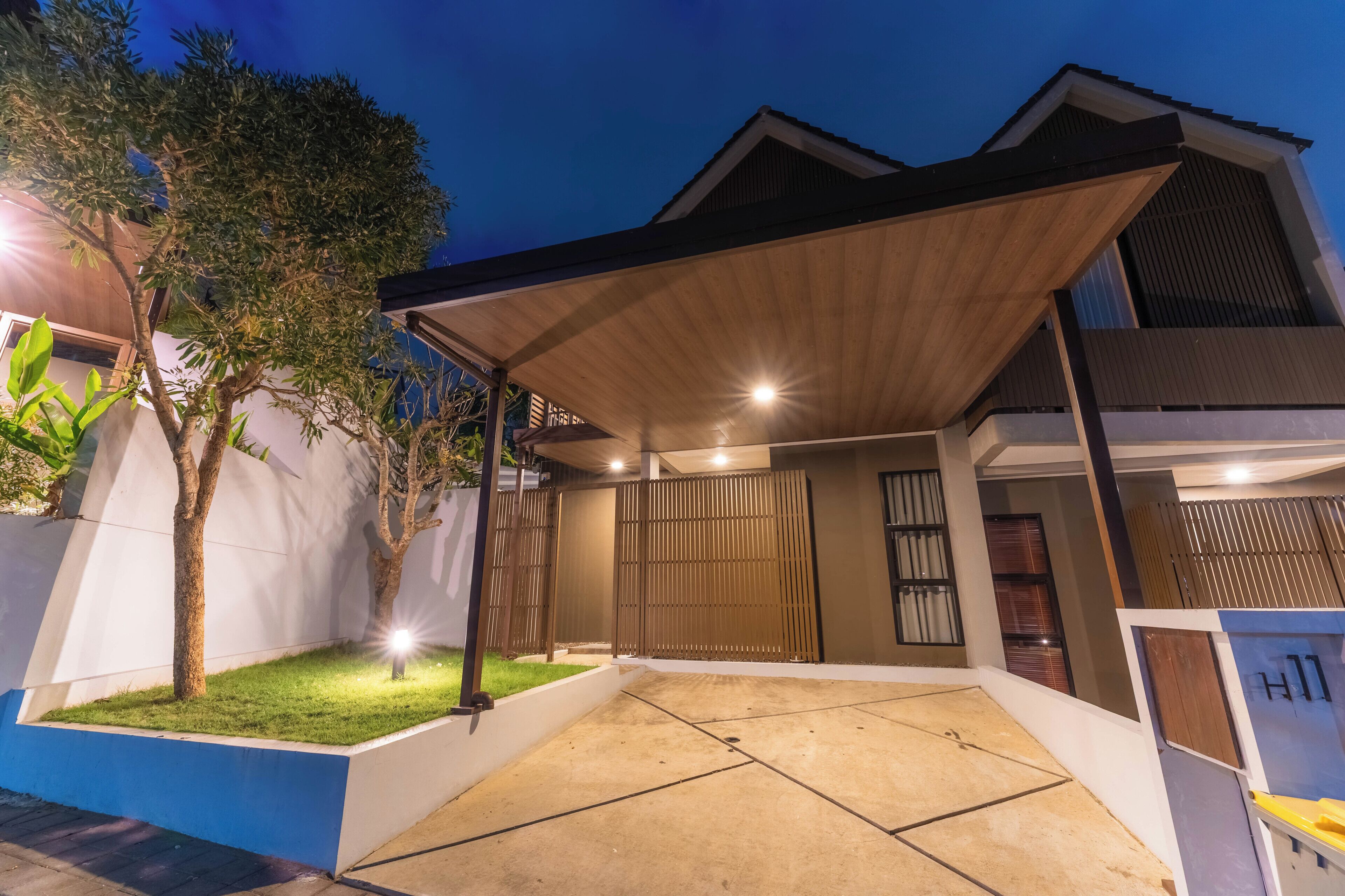 A modern house with a covered patio, a well-maintained lawn, and a gated entrance.
