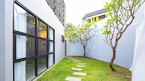 Un sendero estrecho con piedras para pisar que conduce a un edificio con grandes ventanales y un árbol.