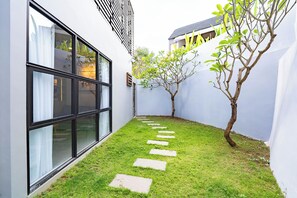 Un sendero estrecho con piedras para pisar que conduce a un edificio con grandes ventanales y un árbol.