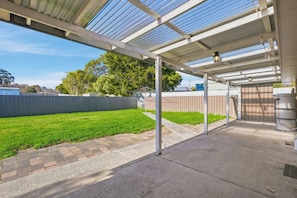 A covered outdoor area with a concrete floor, a metal fence, and a grassy yard.