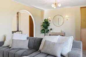A living room with a grey sofa, a round mirror, a plant, and a wooden cabinet.