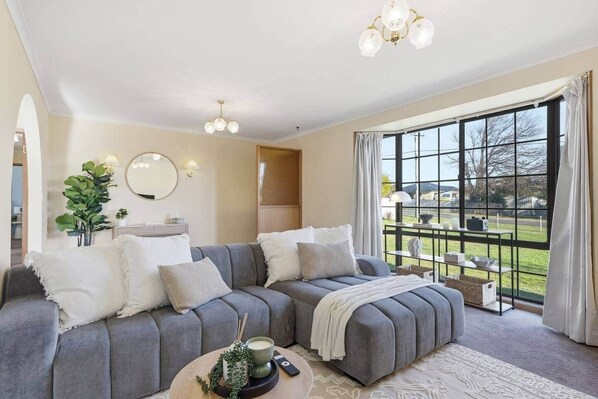 A modern living room with a grey sectional sofa, a round coffee table, and a large window with a view of a park.