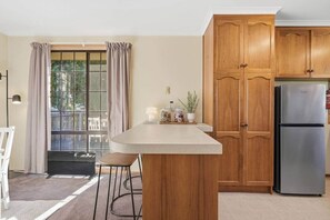 A kitchen with wooden cabinets, a stainless steel refrigerator, a window with curtains, and a small island with stools.