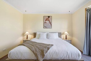 A hotel room with a large bed, two bedside lamps, a framed artwork on the wall, and a window with curtains.