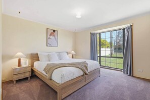 Una camera da letto con un letto grande, un comodino, una lampada, un quadro appeso al muro e una finestra con tende.