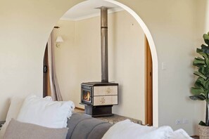A room with a wood-burning stove, a bed with white bedding, and a potted plant.