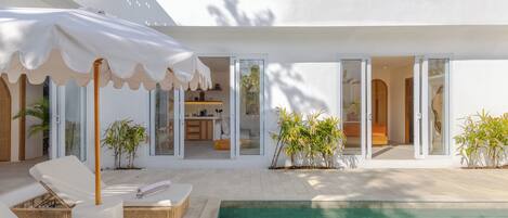 Una casa moderna con piscina, tumbonas y un patio cubierto.