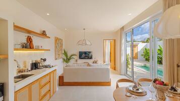 Una habitación de hotel moderna con una cama grande, un área de comedor con una mesa dispuesta para dos personas y vistas a una piscina.