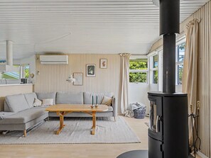 Ein modernes Wohnzimmer mit einer Couch, einem Holztisch, einem schwarzen Herd und einem Fenster mit Vorhängen.