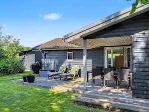 Eine überdachte Terrasse mit Gartenmöbeln, einem Grill und einem Geräteschuppen im Hinterhof.