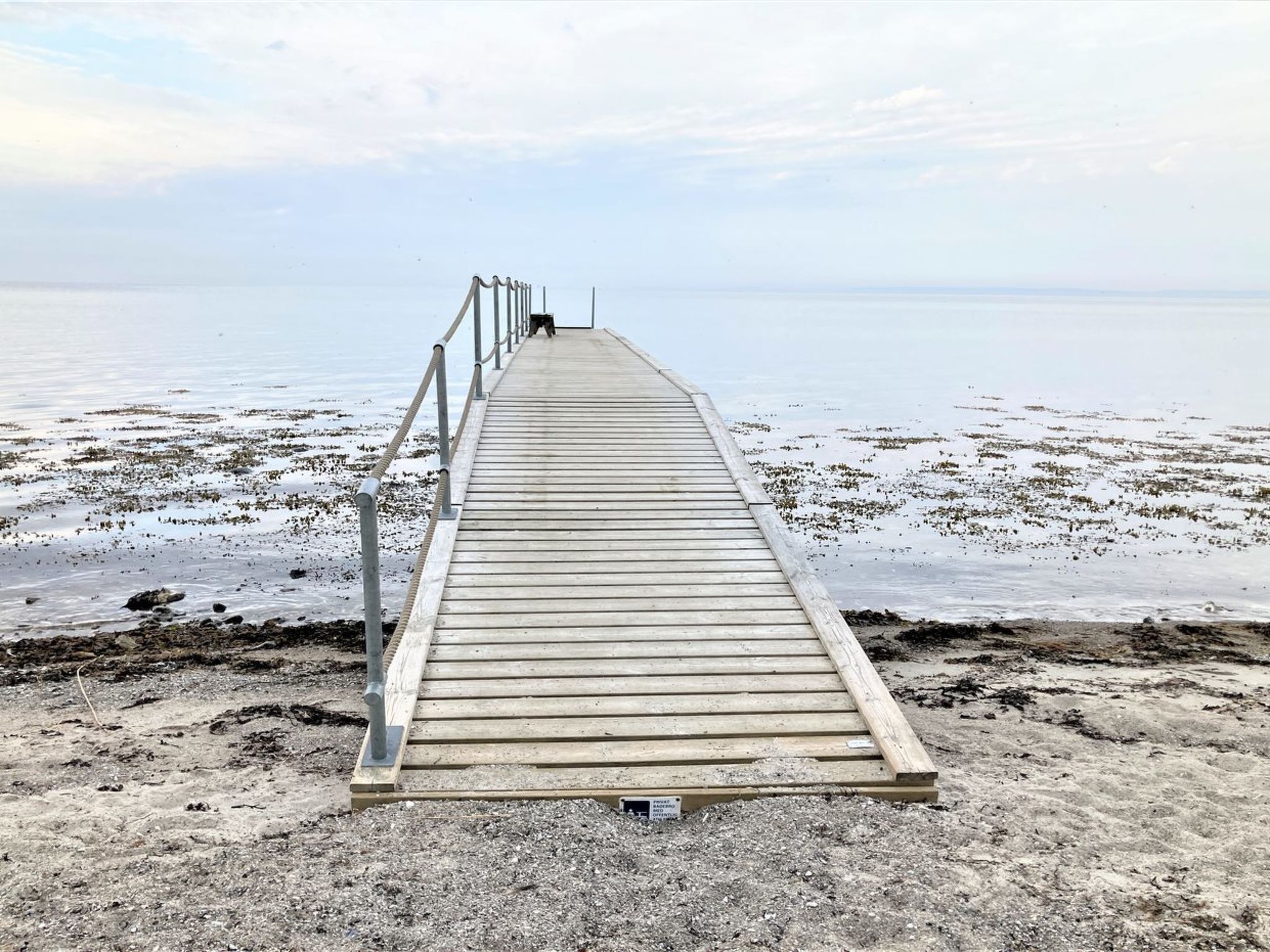 Un muelle de madera que se adentra en una masa de agua tranquila, con una barandilla de metal en un lado.