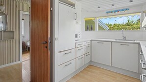 Una cucina moderna con mobili bianchi, una porta in legno e una finestra con vista su del verde.