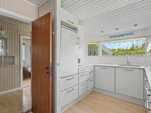 Eine moderne Küche mit weißen Schränken, einer Holztür und einem Fenster mit Blick auf Grünflächen.