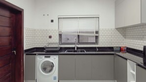 Eine kleine Küche mit Waschmaschine, Spüle und einem Fenster mit Jalousien.