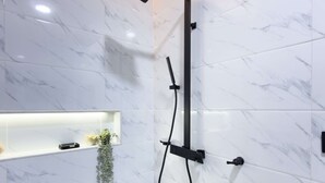 Ein modernes Badezimmer mit Dusche, Marmorwänden und einem Regal mit einer Pflanze.