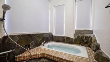 A stone-walled bathroom with a bathtub, a shower, and a window.