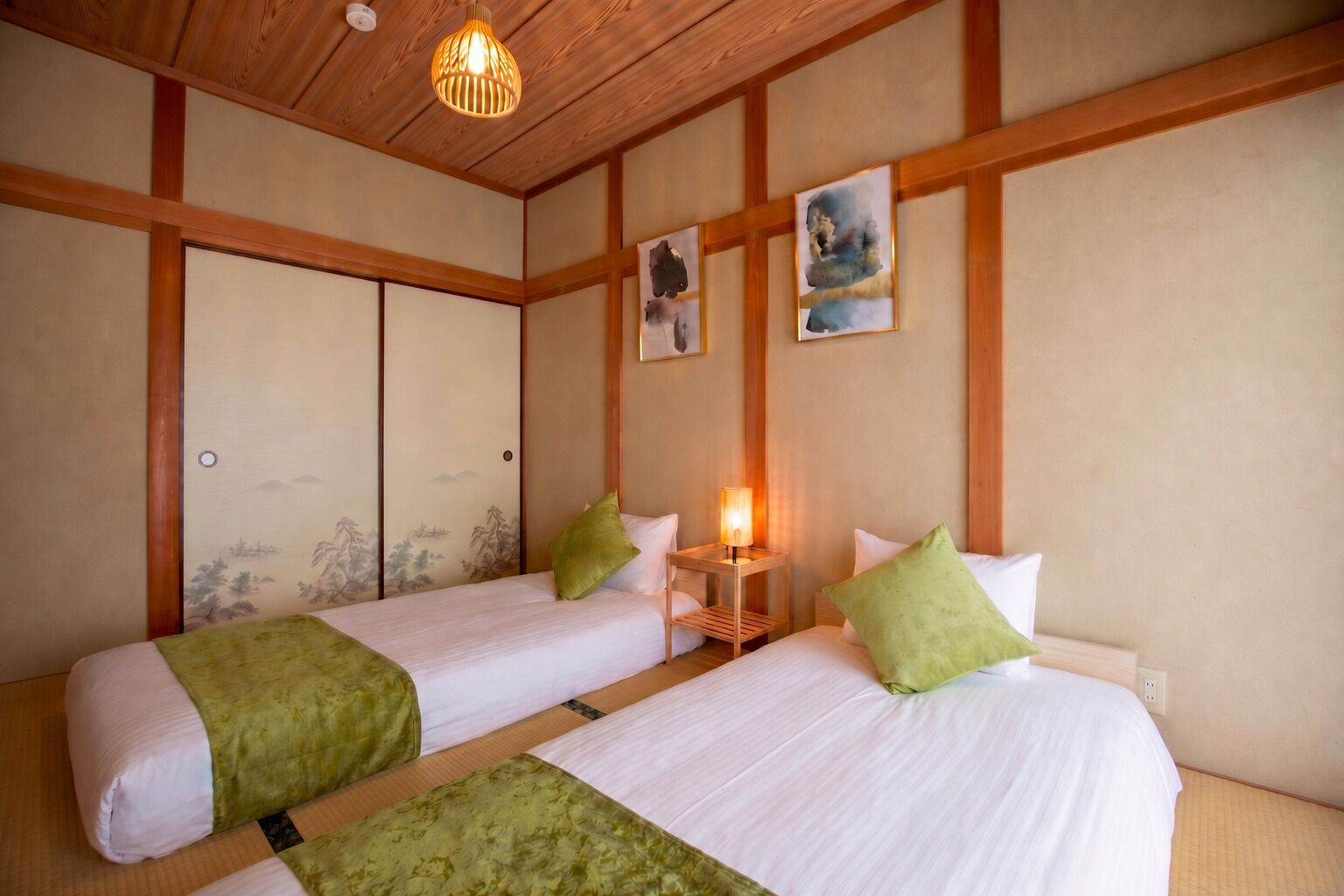 A traditional Japanese-style room with two beds, wooden beams, tatami flooring, and artwork on the walls.