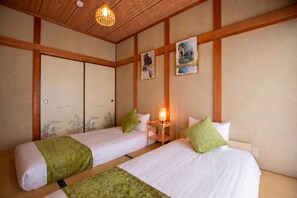 Una habitación tradicional japonesa con dos camas, vigas de madera, suelo de tatami y obras de arte en las paredes.