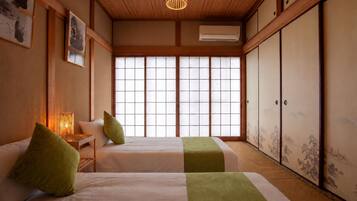 A traditional Japanese-style room with tatami flooring, two beds with green accents, a shoji screen window, and a hanging light fixture.