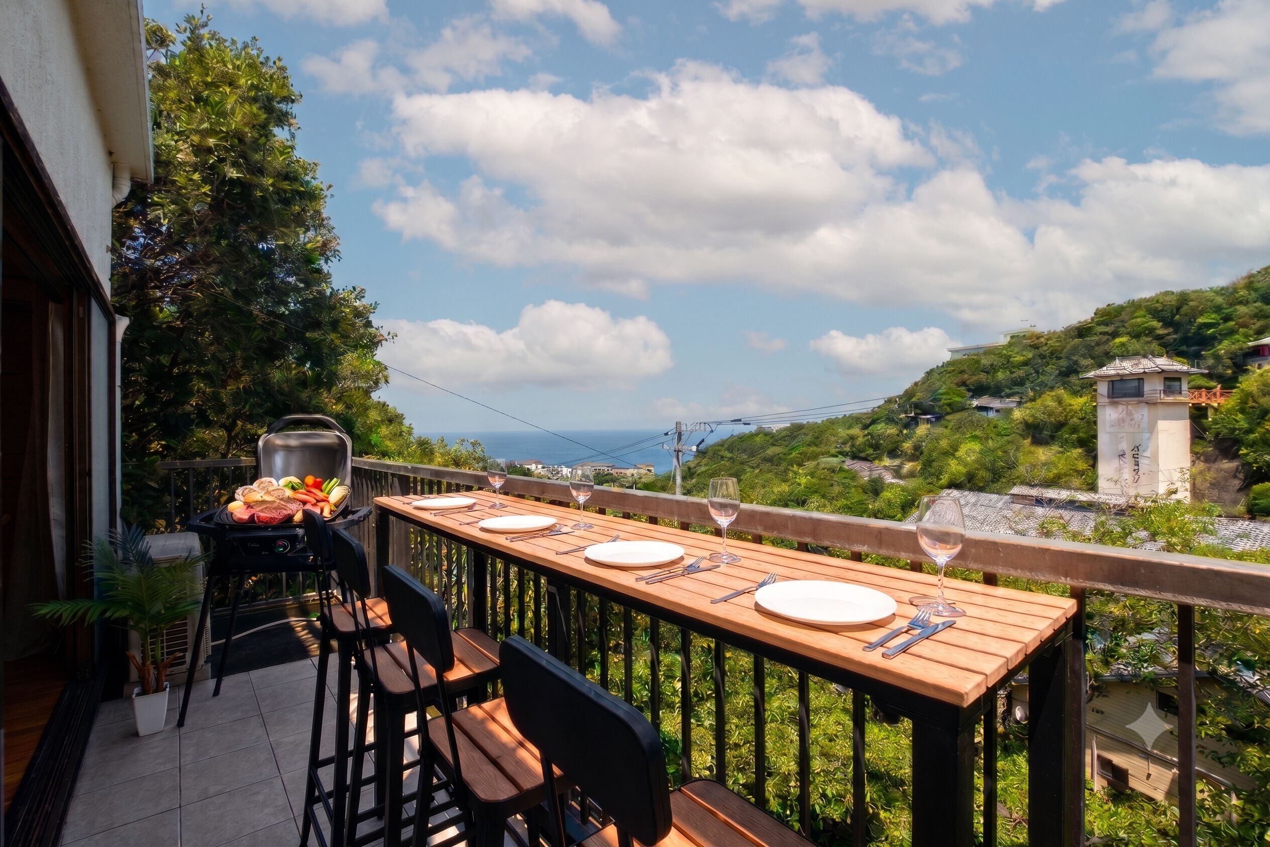 A balcony with a wooden table set for dining, a grill, and a potted plant.