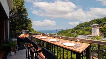 A balcony with a wooden table set for dining, a grill, and a potted plant.