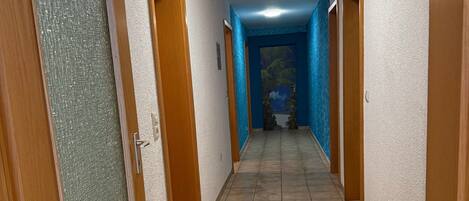 Un pasillo con piso de baldosas, puertas de madera y una pared azul al final.