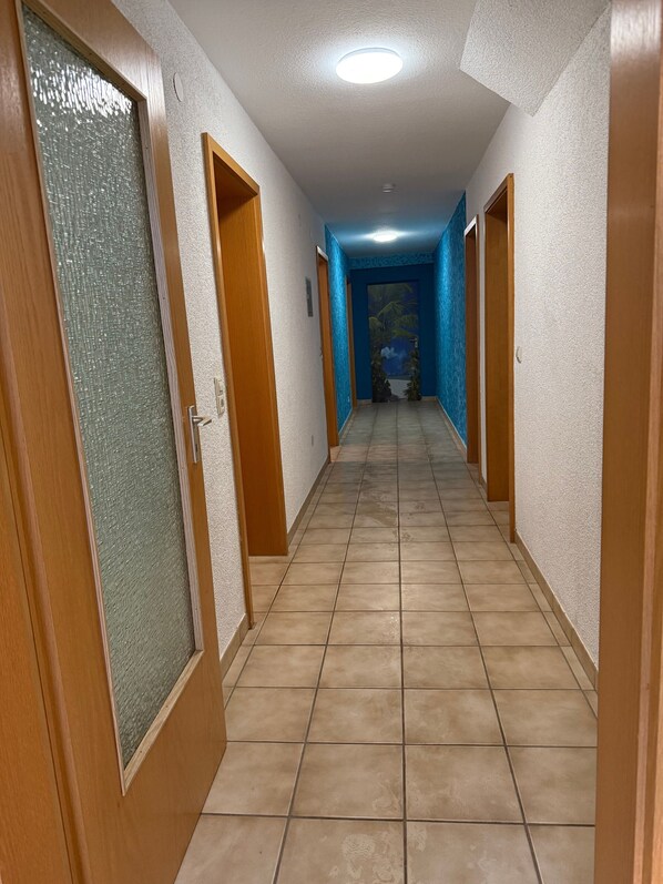 A corridor with tiled flooring, wooden doors, and a blue wall at the end.
