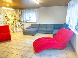 A living room with a sectional sofa, a red armchair, and a wall covered with books and papers.