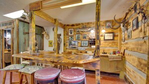 Un intérieur rustique avec un bar en bois, des tabourets et divers trophées d’animaux ainsi que des tableaux accrochés aux murs.