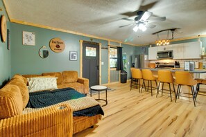 A living room with a sofa, a coffee table, and a dining area with bar stools. - Cookout Patio w/ Fireplace! Norfork Lake Cabin (Elizabeth)