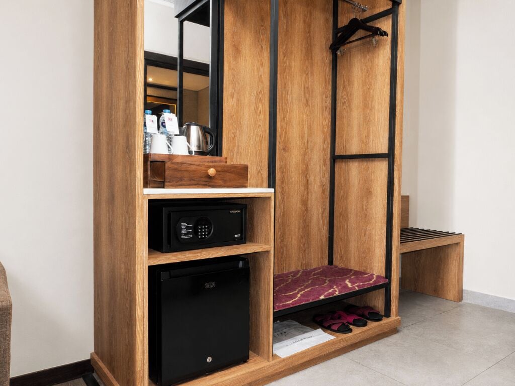 Una habitación compacta con microondas incorporado, un refrigerador pequeño, un banco de madera y un espejo.