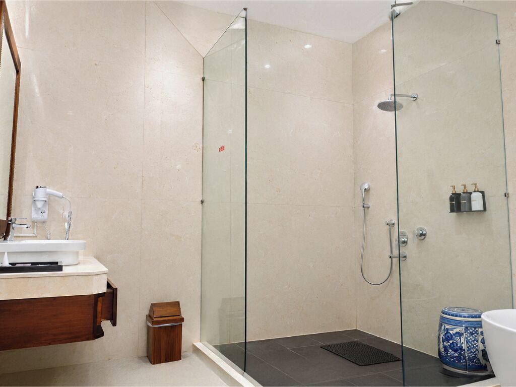 A modern bathroom with a glass-enclosed shower, a wooden vanity, and a small trash bin.