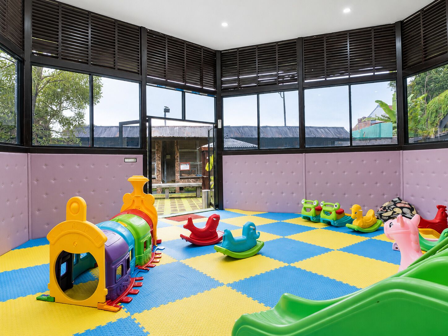 A play area with a train set and various toys, surrounded by large windows and a checkered floor.