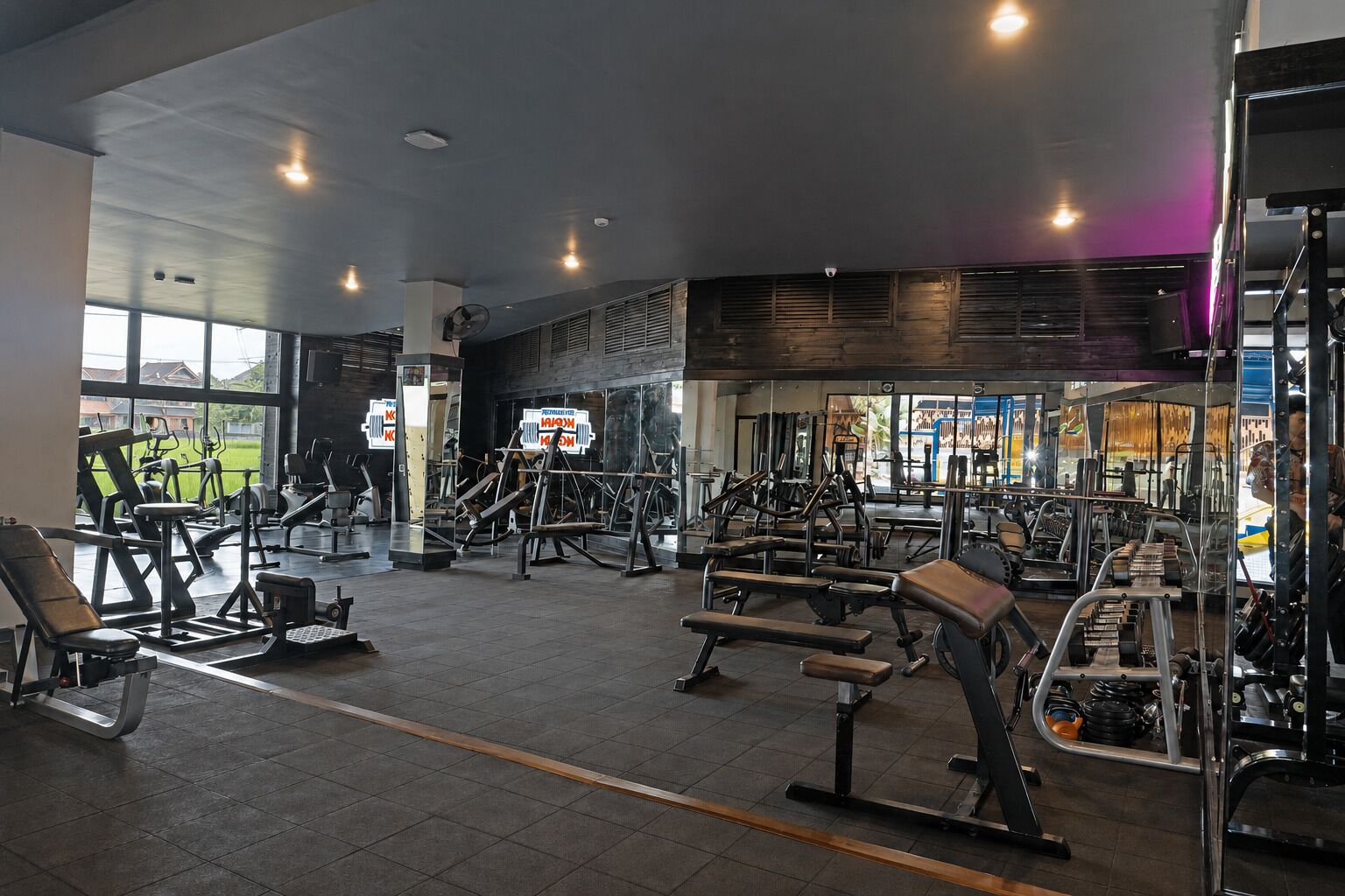 Un gimnasio con diferentes equipos de ejercicio, amplias ventanas y vistas al exterior.