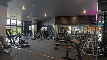 Un gimnasio con diferentes equipos de ejercicio, amplias ventanas y vistas al exterior.