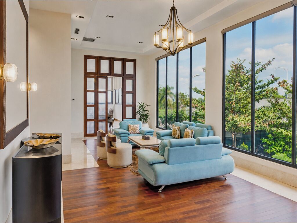 A spacious living room with a large window, a blue sofa set, and a modern chandelier.