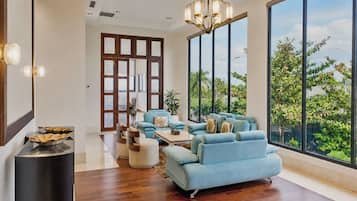 A spacious living room with a large window, a blue sofa set, and a modern chandelier.