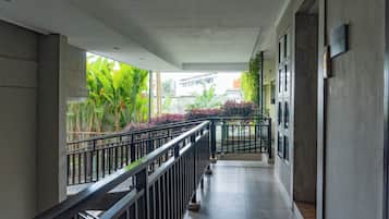 A corridor with a tiled floor, a metal railing, and a view of greenery outside.